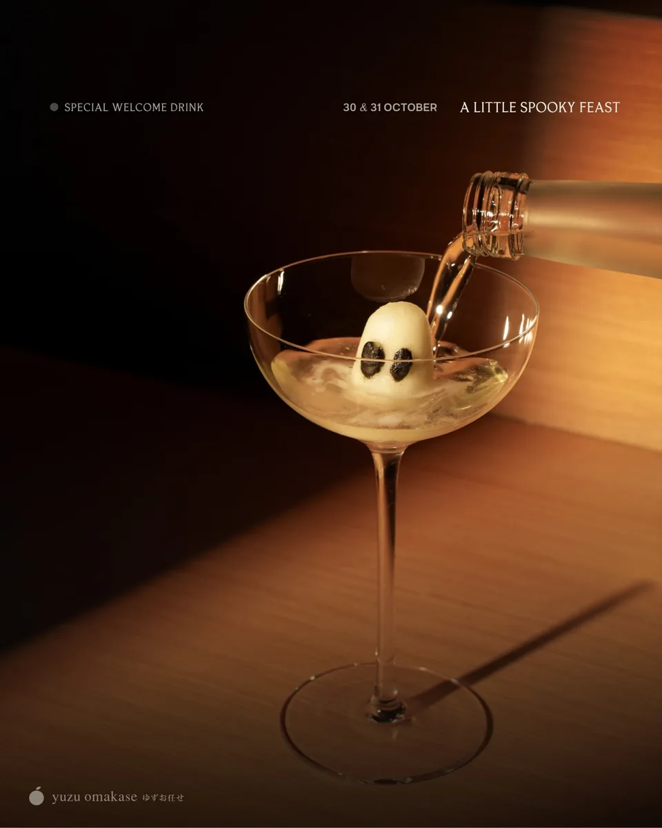 Yuzu Omakase Halloween poster: A LITTLE SPOOKY FEAST, SPECIAL WELCOME DRINK, 30 & 31 OCTOBER, ghost-shaped ice sphere in a coupe cocktail glass on black background with yuzu omakase branding