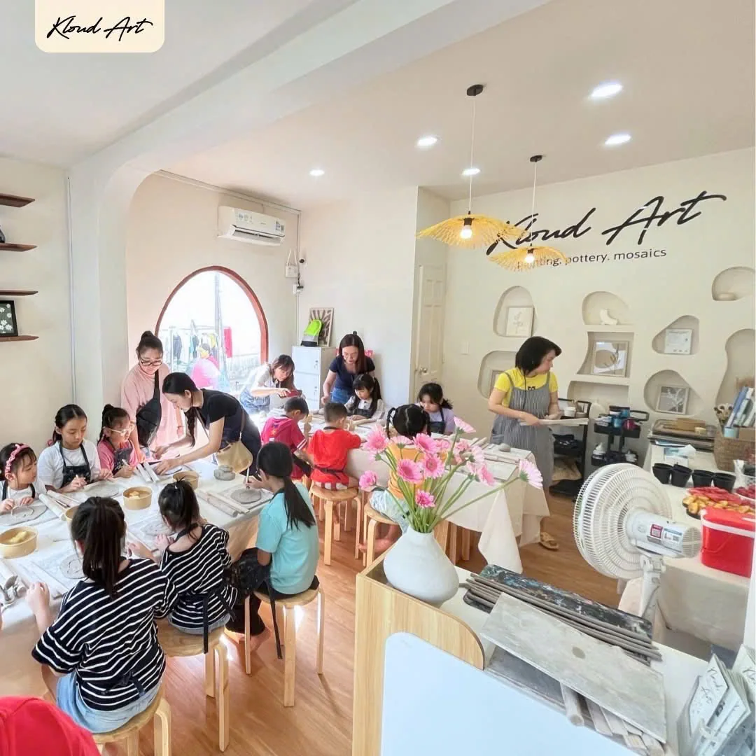 Children and a teacher working at clay tables inside the Kloud Art Thao Dien studio